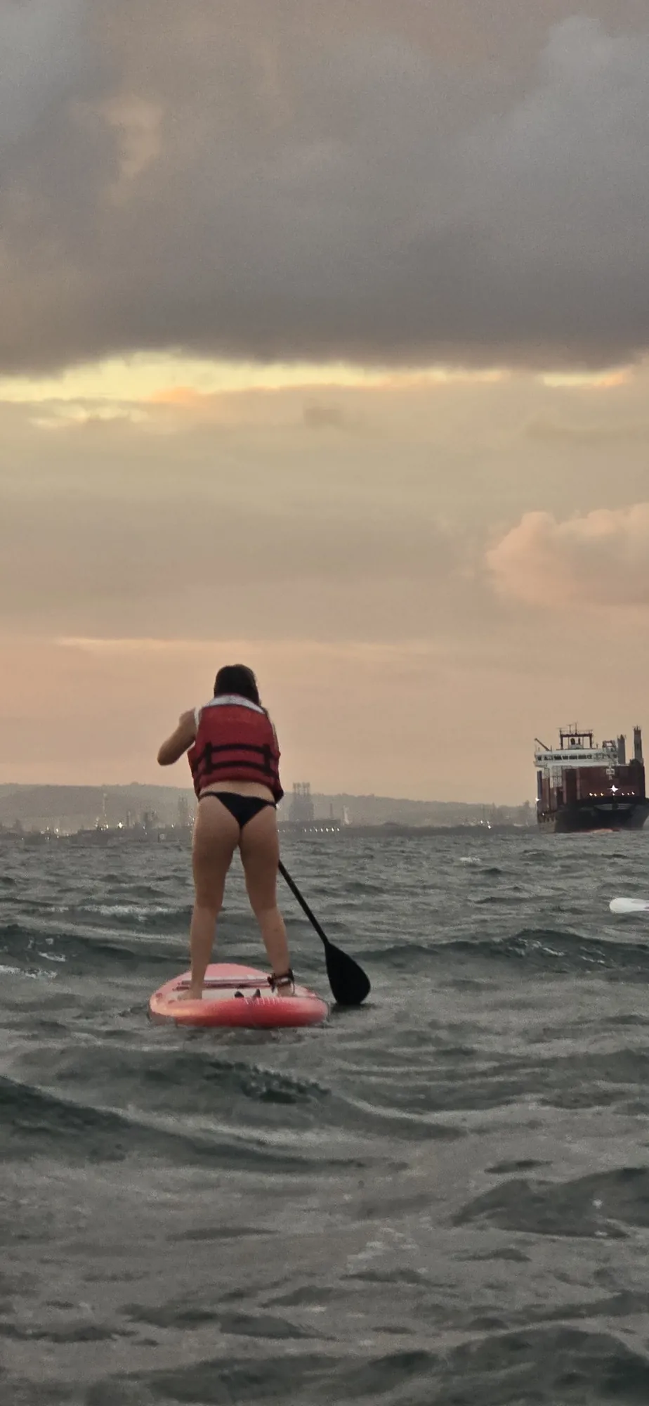 Persona entrando al mar con tabla de paddleboard durante la hora dorada en Playa Las Velas, Cartagena